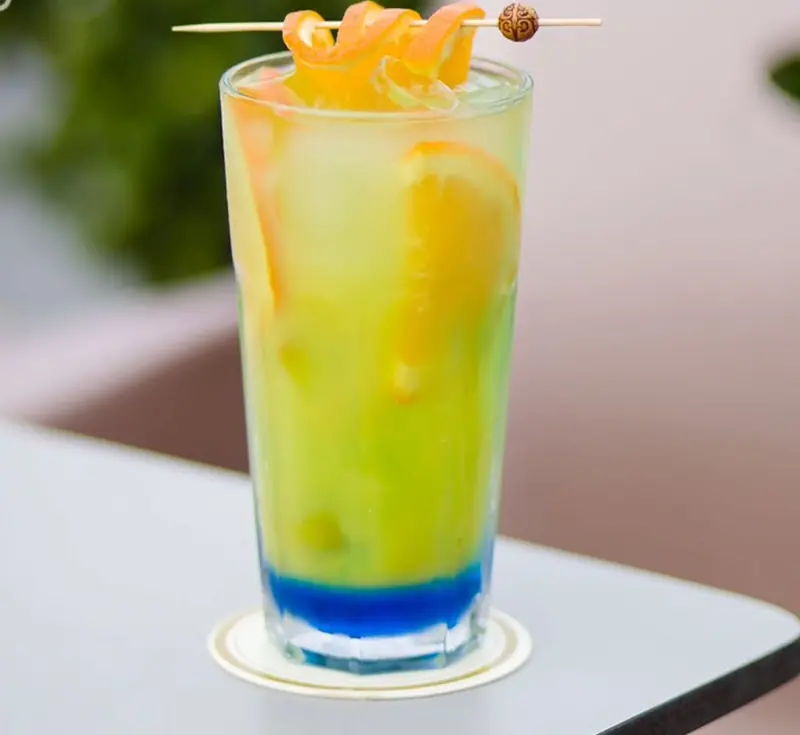 Un cooler à l'orange au fond bleu, zeste en spirale piqué sur pic de bois, sur une table de la terrasse