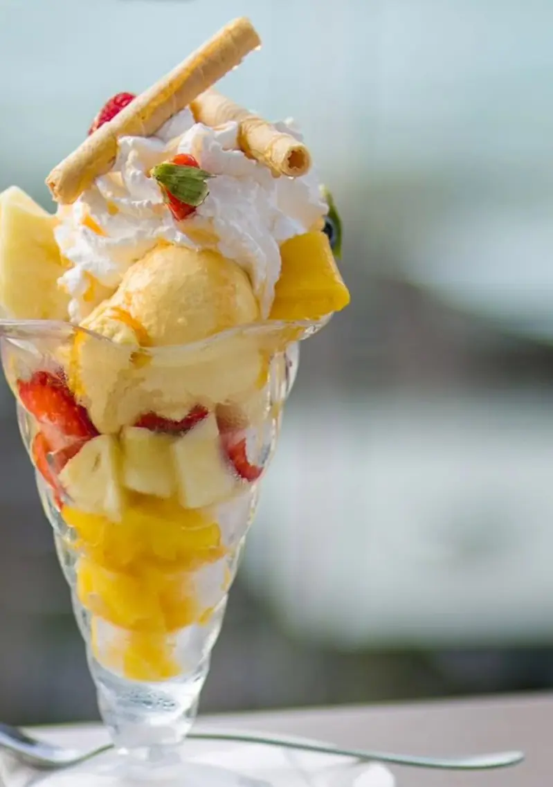 Coupe glacée aux fruits : glace mangue, ananas, fraises et chantilly, la mer floue derrière