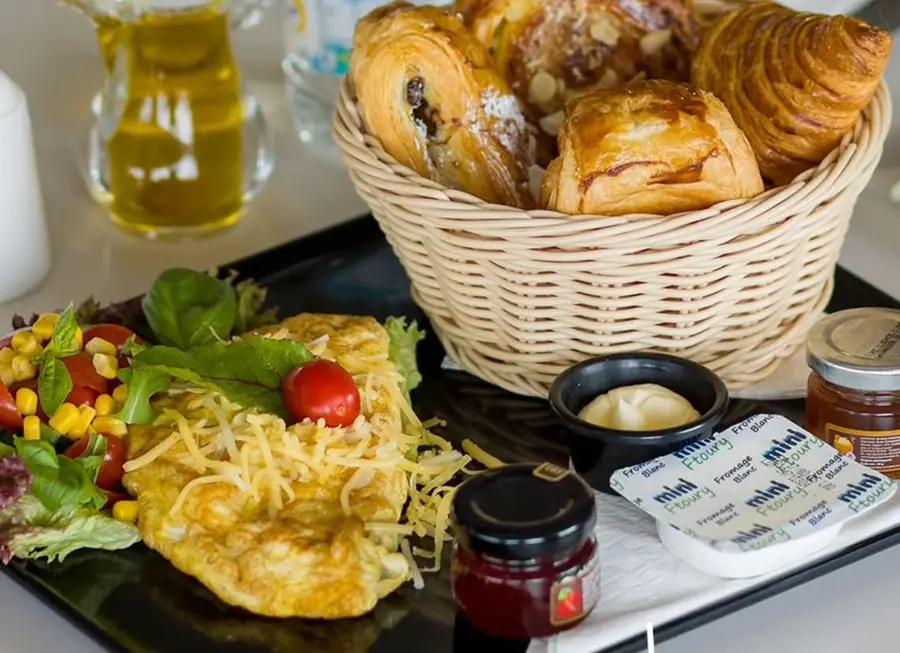 Plateau du petit-déjeuner : panier de viennoiseries, omelette au fromage, salade, huile d'olive et confitures