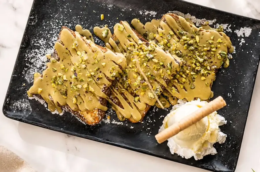 Pain perdu nappé de crème de pistache et pistaches concassées sur plat d'ardoise, chantilly et cigarette russe