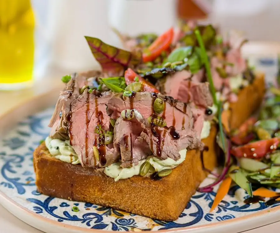 Tranches de rosbif rosé sur brioche toastée et crème aux herbes, graines de courge, sur assiette à motifs bleus