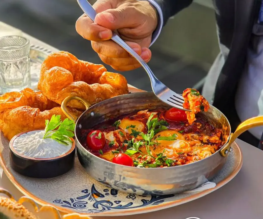 Shakshuka aux œufs et tomates cerises servie dans sa poêle en cuivre martelé, beignets dorés et fromage frais