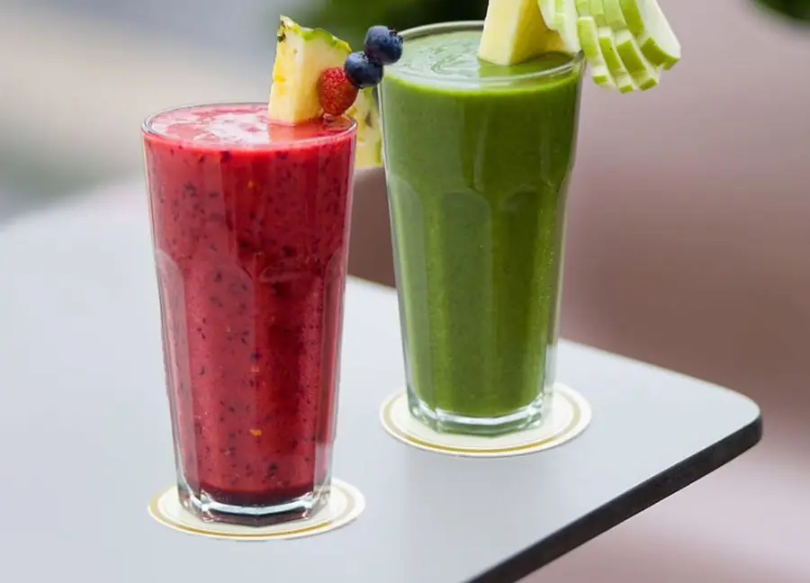 Deux smoothies, fruits rouges et vert aux fruits frais, garnis d'ananas, fraise et myrtilles