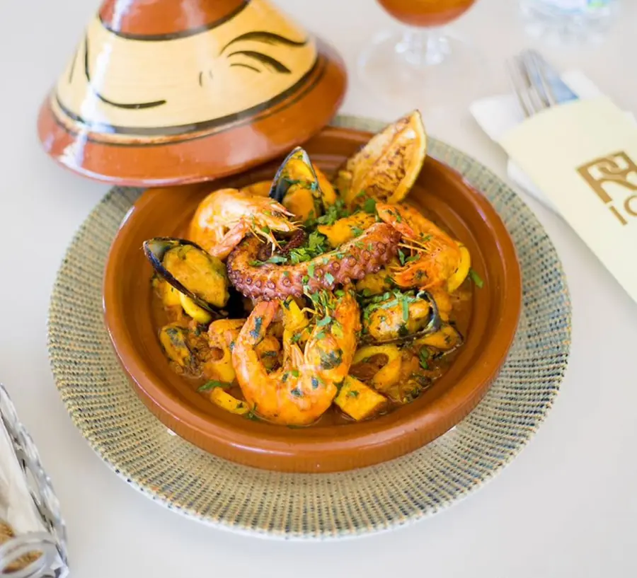Tajine de la mer : crevettes, moules et poulpe dans un plat en terre cuite, serviette brodée RR Ice à côté